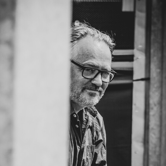 Black and white photograph of author Charlie Higson, he is a middle aged white man wearing glasses.