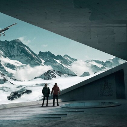 Photo of 007 Elements in Solden Austria. Image shows two people looking out onto a snowy mountain range with a Land Rover and plane in the distance