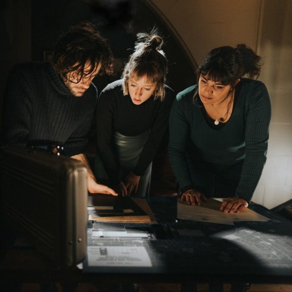 Photo of three people playing the Shadow of SPECTRE game by Hidden City. The image shows three white skinned young people looking at some files and clues on a table.