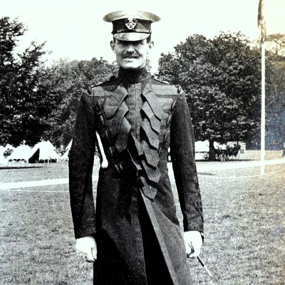 Black and white photograph of Valentine Fleming in uniform with army tents and flagpole in background