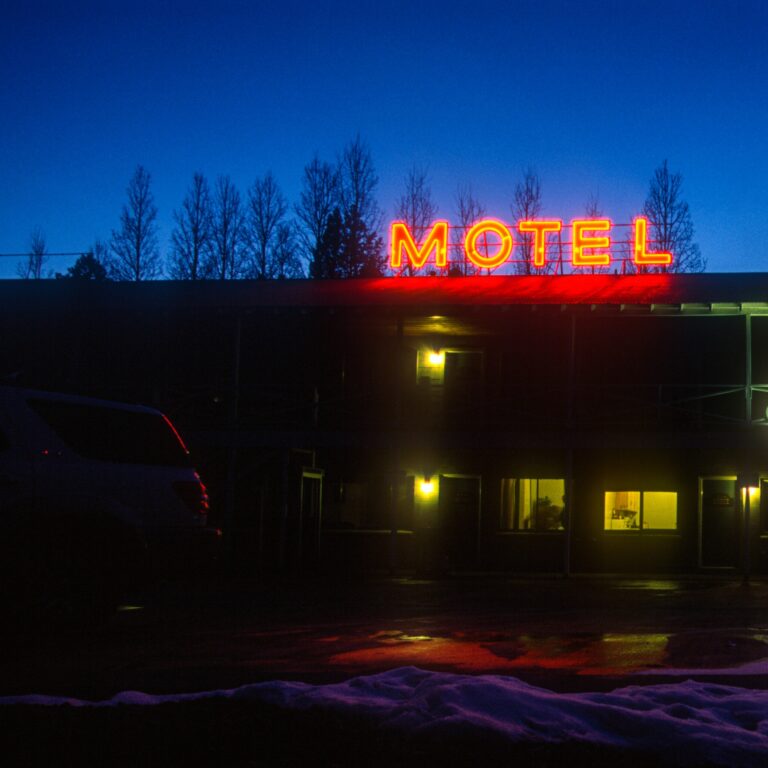 Photograph of a motel at night, with glowing neon sign.