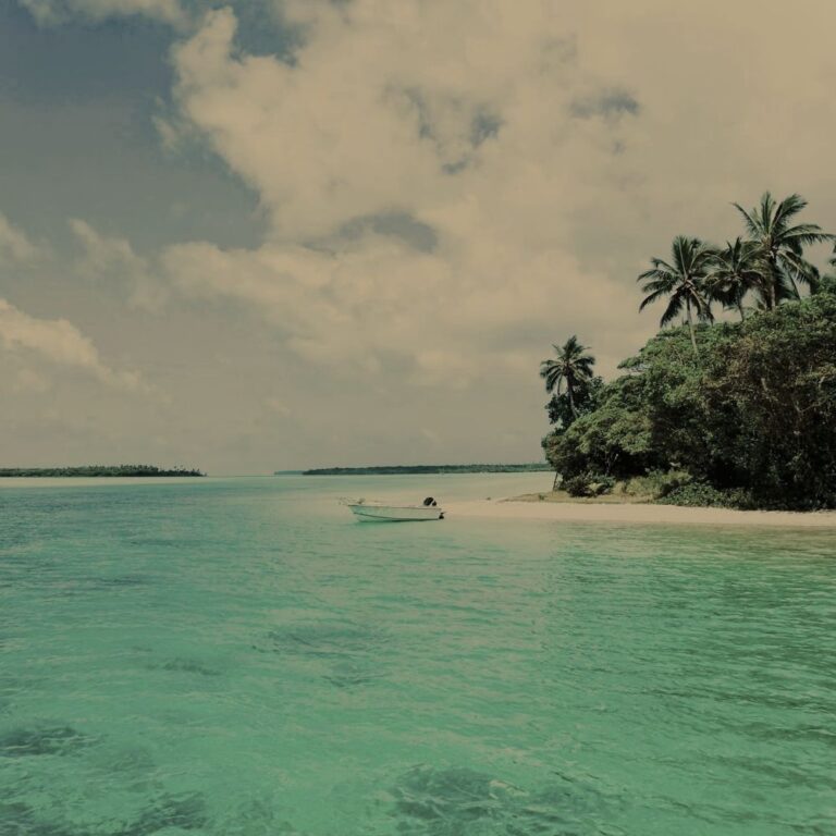 Small boat off white sandy isnad in tropical sea
