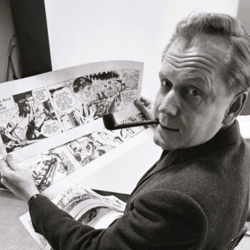 Picture of a man with a pipe showing his comic strip drawings at a desk