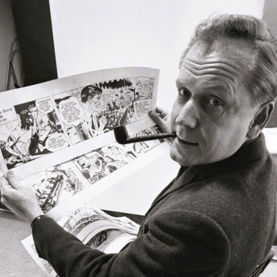 Picture of a man with a pipe showing his comic strip drawings at a desk